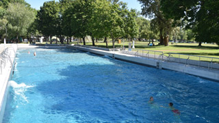 Schwimmbecken im Freien mit wellendem Wasser, rundherum Bume